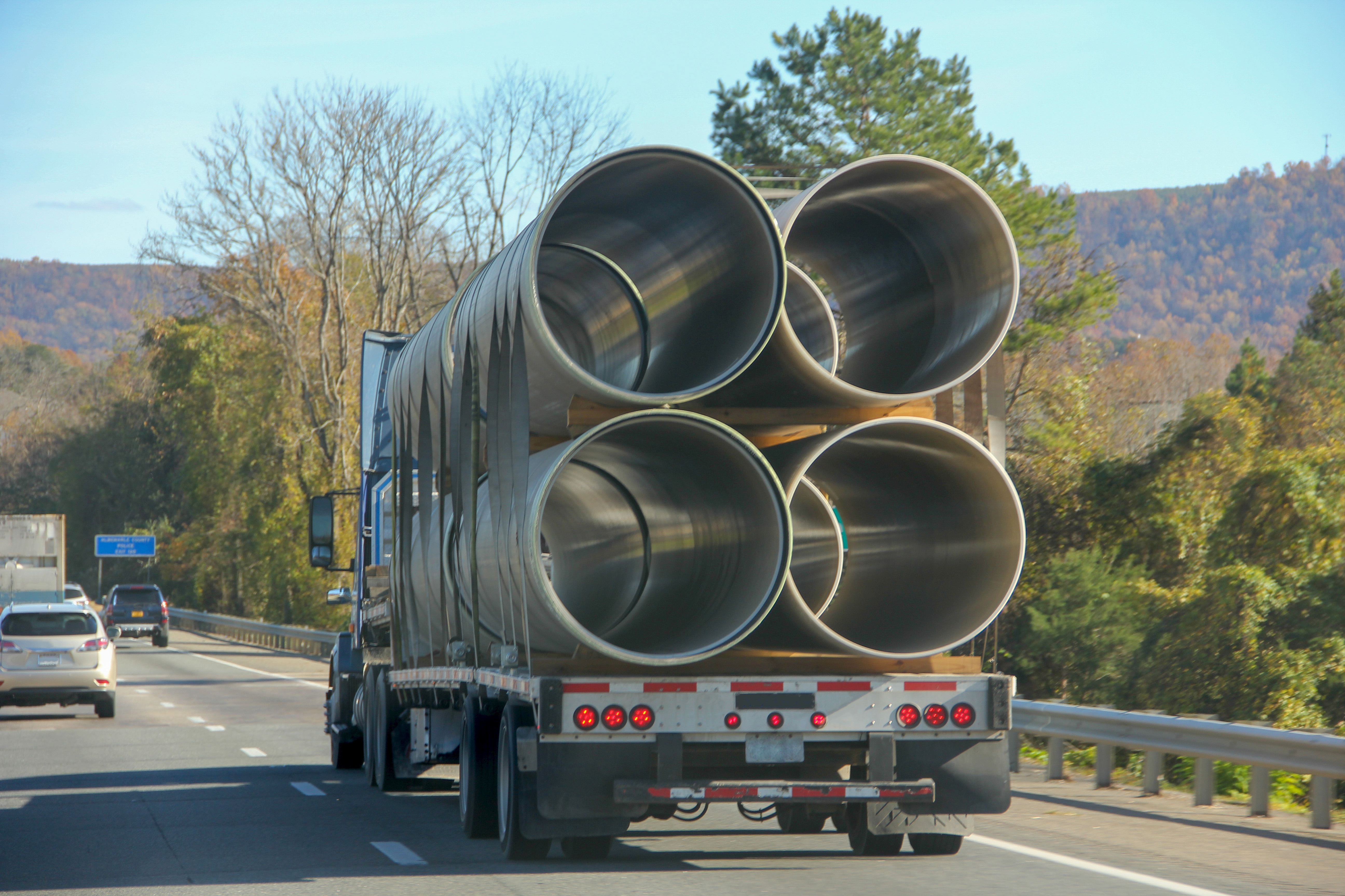 A flatbed truck carrying big size metallic cylinder pipes in the interstate.